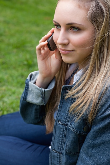 Молодая блондинка женщина, вызов ее мобильный телефон, сидя в парке