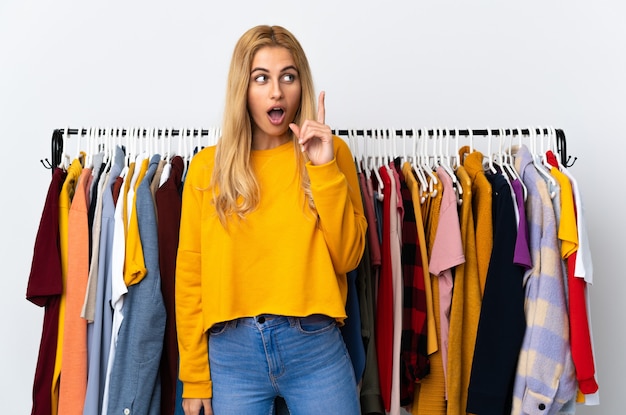 Young blonde woman in a clothing store thinking an idea pointing the finger up