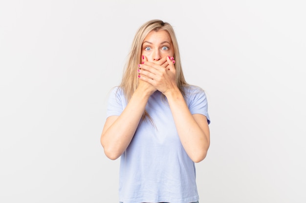 Young blonde woman covering mouth with hands with a shocked