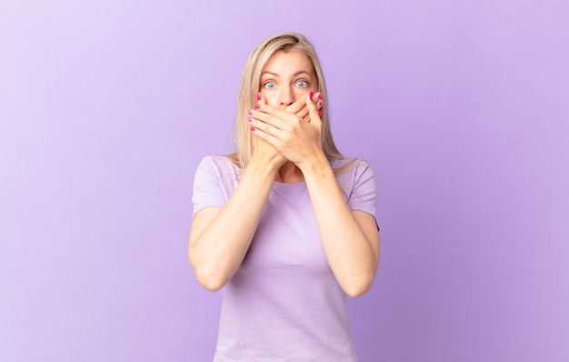 Young blonde woman covering mouth with hands with a shocked