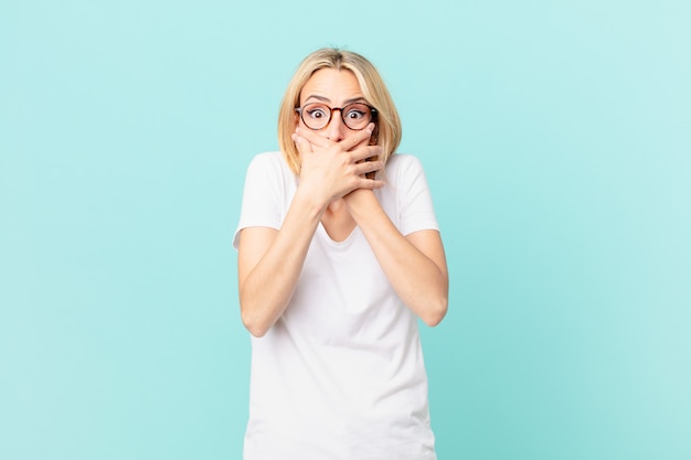 Giovane donna bionda che copre la bocca con le mani con uno shock