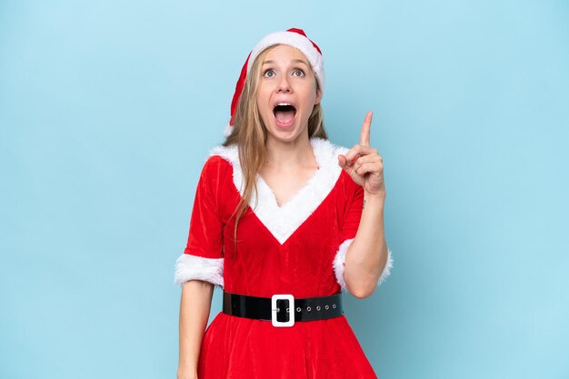 Young blonde woman dressed as mama claus isolated on blue background pointing up and surprised
