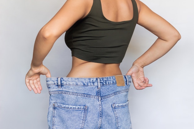 A young blonde woman dressed in wide jeans standing with her back demonstrating successful weight