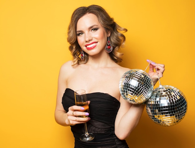 Young blonde woman in evening black dress holding a glass of champagne and disco ball