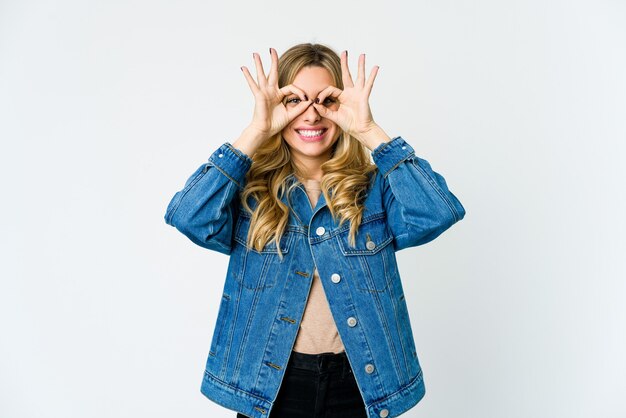 Young blonde woman excited keeping ok gesture on eye