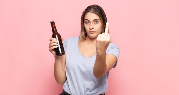 Young blonde woman feeling angry, annoyed, rebellious and aggressive, flipping the middle finger, fighting back