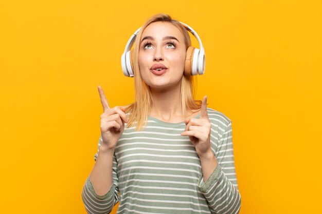 Young blonde woman feeling awed and open mouthed pointing upwards with a shocked and surprised look