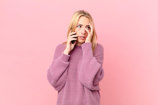 Giovane donna bionda che si sente annoiata, frustrata e assonnata dopo una noiosa e parlando con uno smartphone