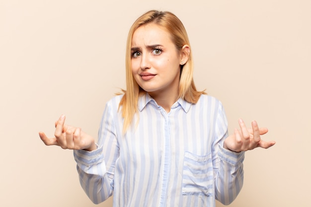 Young blonde woman feeling clueless and confused, having no idea, absolutely puzzled with a dumb or foolish look