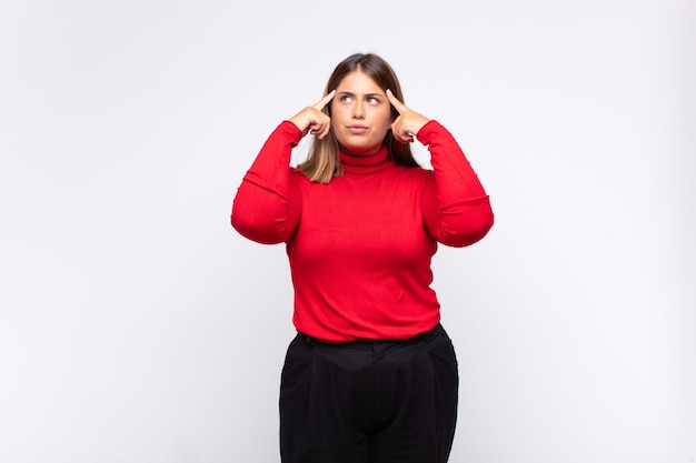 Young blonde woman feeling confused or doubting, concentrating on an idea, thinking hard, looking to copy space on side