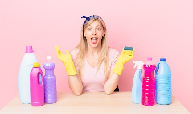 Young blonde woman feeling happy and astonished at something unbelievable. housekeeper concept