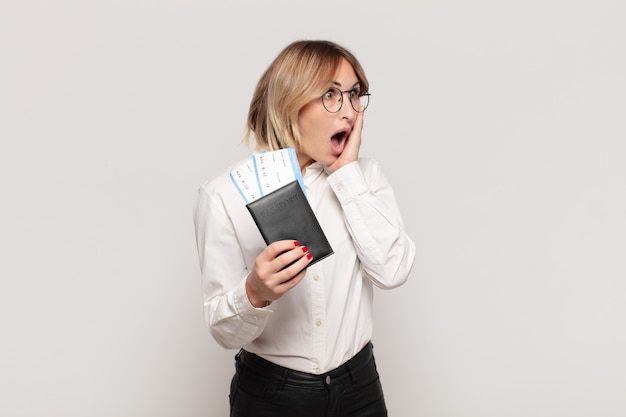 Young blonde woman feeling happy, excited and surprised, looking to the side with both hands on face