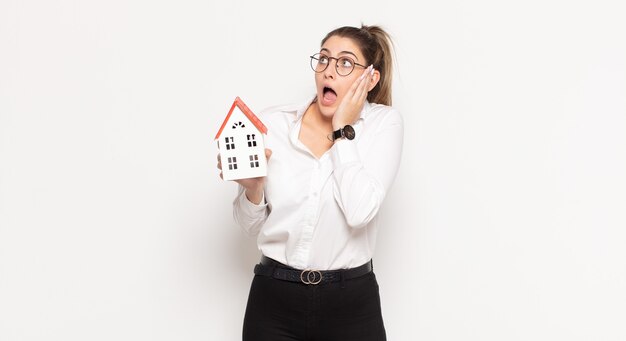 Young blonde woman feeling happy, excited and surprised, looking to the side with both hands on face