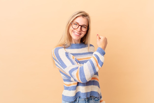 Young blonde woman feeling happy and facing a challenge or celebrating