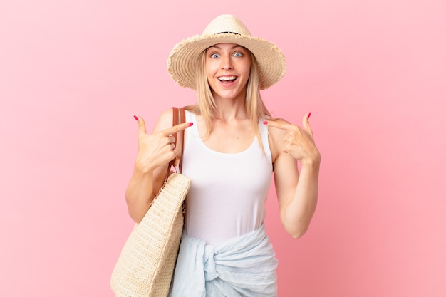 Young blonde woman feeling happy and pointing to self with an excited