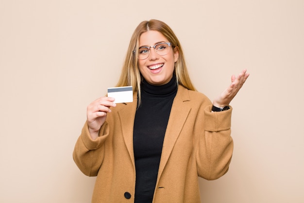 Giovane donna bionda sentirsi felice, sorpresa e allegra, sorridendo con atteggiamento positivo, realizzando una soluzione o un'idea con una carta di credito