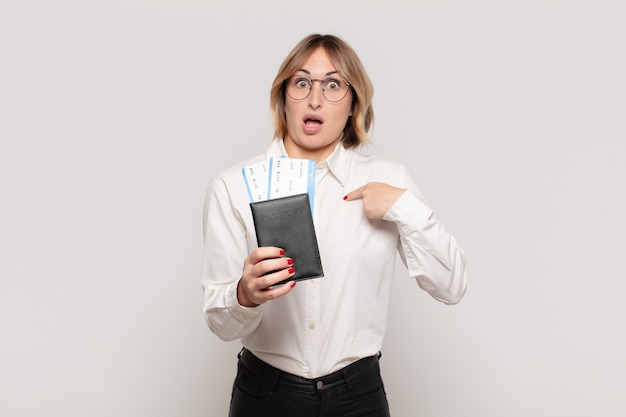 Young blonde woman feeling happy, surprised and proud, pointing to self with an excited, amazed look