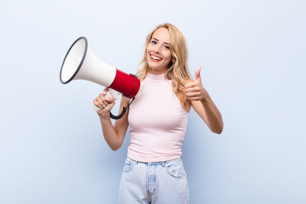 Giovane donna bionda sentirsi orgogliosa, spensierata, fiduciosa e felice, sorridendo positivamente con il pollice in alto con un megafono