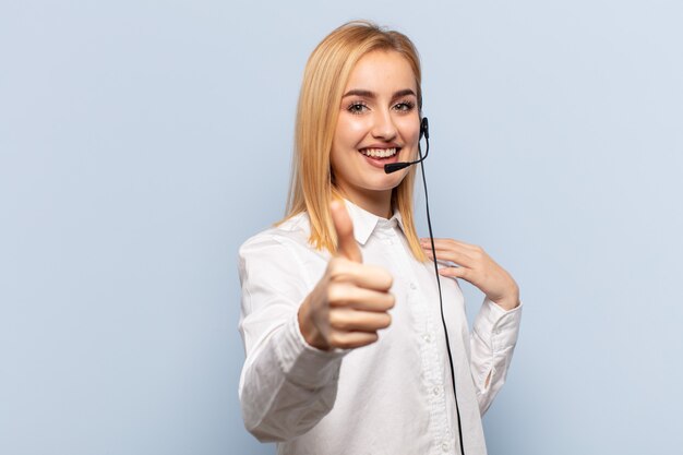 young blonde woman feeling proud, carefree, confident and happy, smiling positively with thumbs up