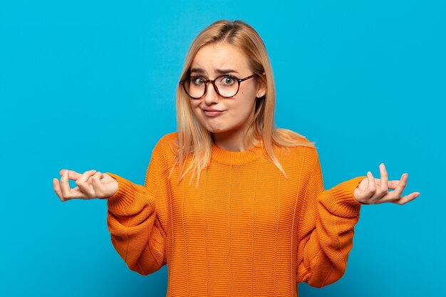 Young blonde woman feeling puzzled and confused, doubting, weighting or choosing different options with funny expression