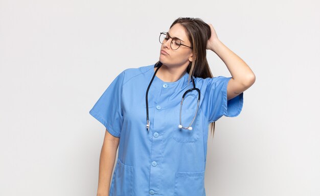 Young blonde woman feeling puzzled and confused, scratching head and looking to the side