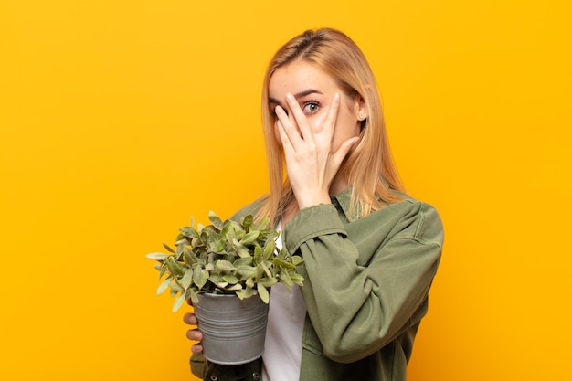 Young blonde woman feeling scared or embarrassed, peeking or spying with eyes half-covered with hands