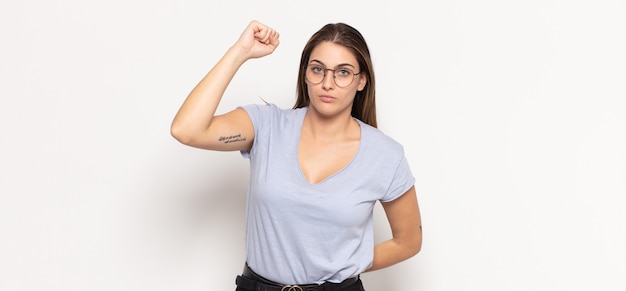 Young blonde woman feeling serious, strong and rebellious, raising fist up, protesting or fighting for revolution