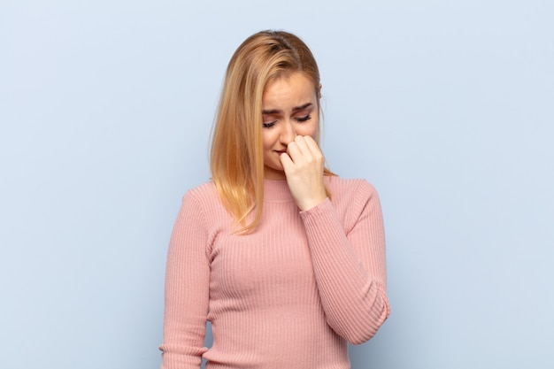 Young blonde woman feeling serious, thoughtful and concerned, staring sideways with hand pressed against chin