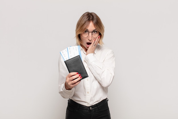 young blonde woman feeling shocked and scared, looking terrified with open mouth and hands on cheeks