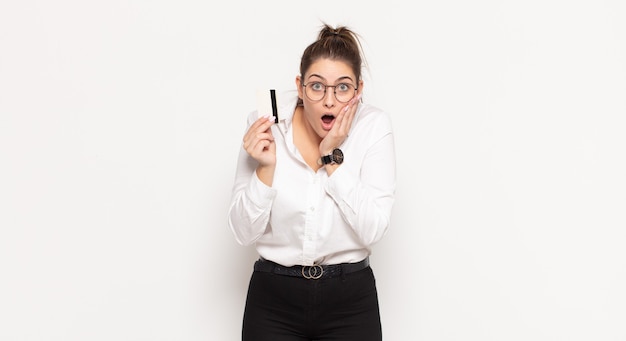 Young blonde woman feeling shocked and scared, looking terrified with open mouth and hands on cheeks