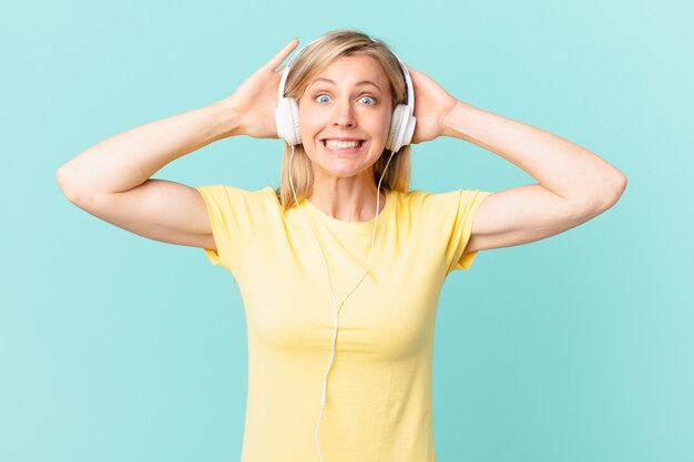 Photo young blonde woman feeling stressed, anxious or scared, with hands on head and listening music.