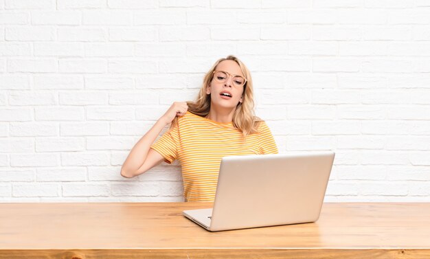 Young blonde woman feeling stressed, anxious, tired and frustrated, pulling shirt neck, looking frustrated with problem using a laptop