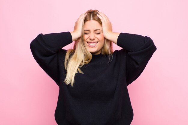 Young blonde woman feeling stressed and frustrated, raising hands to head, feeling tired, unhappy and with migraine over wall