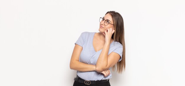 Young blonde woman feeling thoughtful, wondering or imagining ideas, daydreaming and looking up to copy space