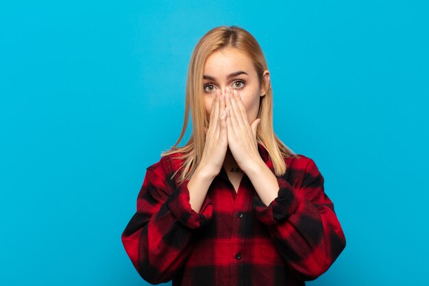 Photo young blonde woman feeling worried, upset and scared, covering mouth with hands, looking anxious and having messed up