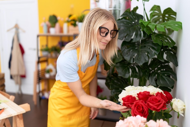 Young blonde woman florist smiling confident touching flowers at flower shop