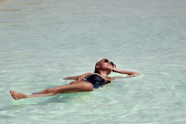 Giovane donna bionda in occhiali e bikini nero rilassante nel mar morto. foto di alta qualità