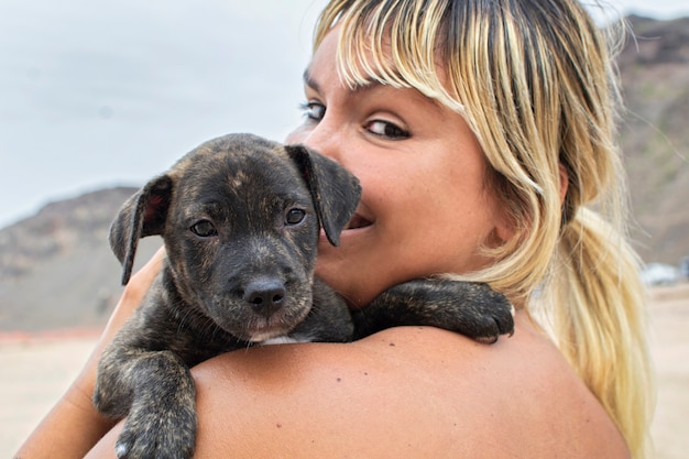 Young blonde woman, happy with her dog puppy caught in her arms.