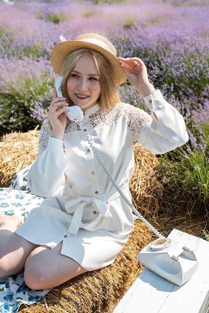 Young blonde woman in hat sitting on lavender field