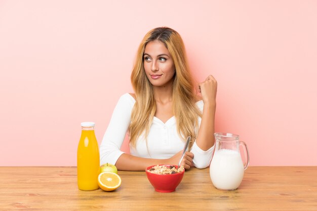 Young blonde woman having breakfast milk standing and looking to the side