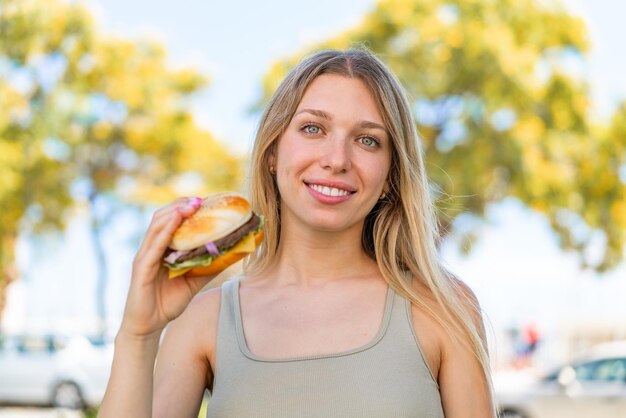 写真 屋外でたくさんの笑顔でハンバーガーを保持している若いブロンドの女性