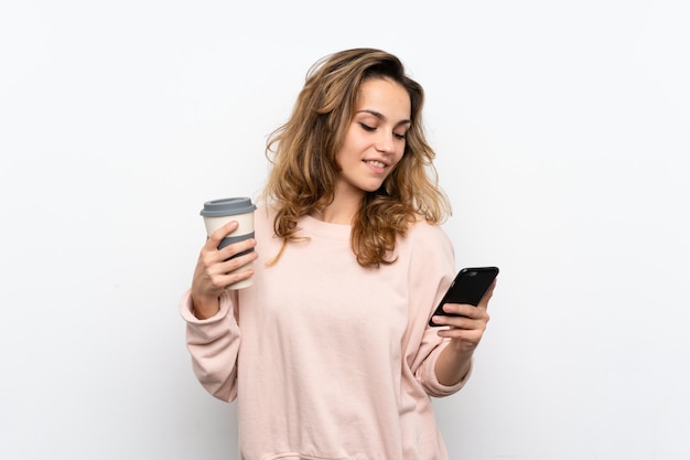 Giovane donna bionda che tiene caffè da portare via e un cellulare