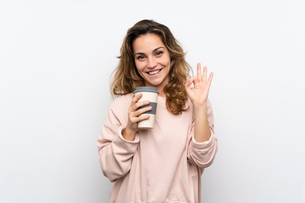 Young blonde woman holding coffee to take away while making OK sign