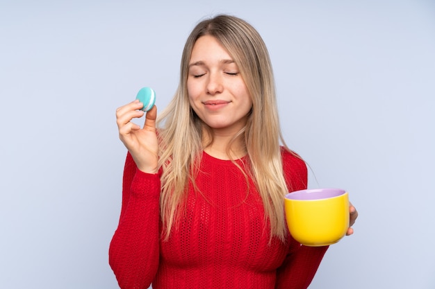 Young blonde woman holding colorful French macarons and a cup of milk