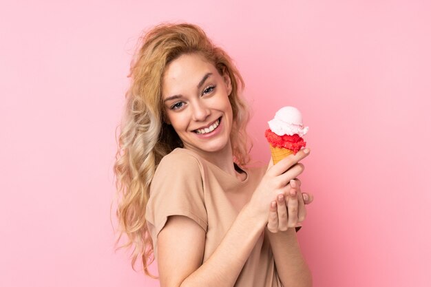 Young blonde woman holding a cornet ice cream isolated on pink wall