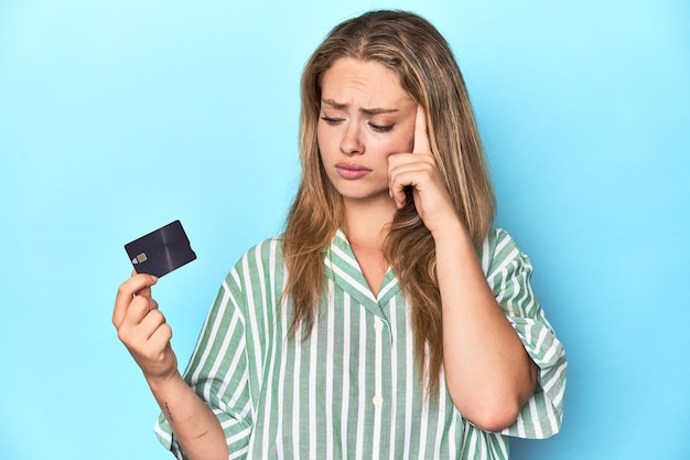 Young blonde woman holding a credit card in a studio