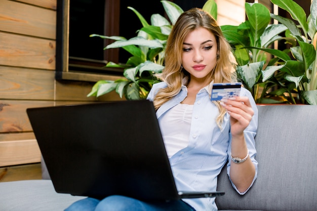 Young blonde woman holding credit card and using laptop computer.