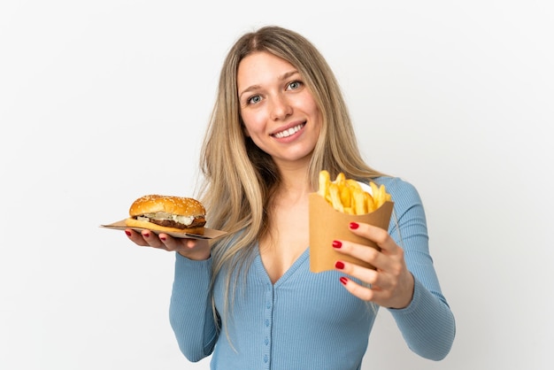 Фото Молодая блондинка женщина, держащая жареные чипсы и чизбургер на изолированном фоне