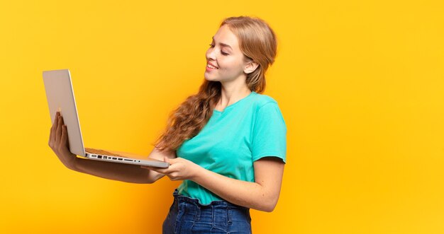 Young blonde woman holding laptop on yellow