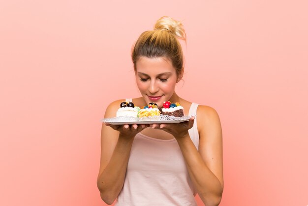 Young blonde woman holding lots of different mini cakes